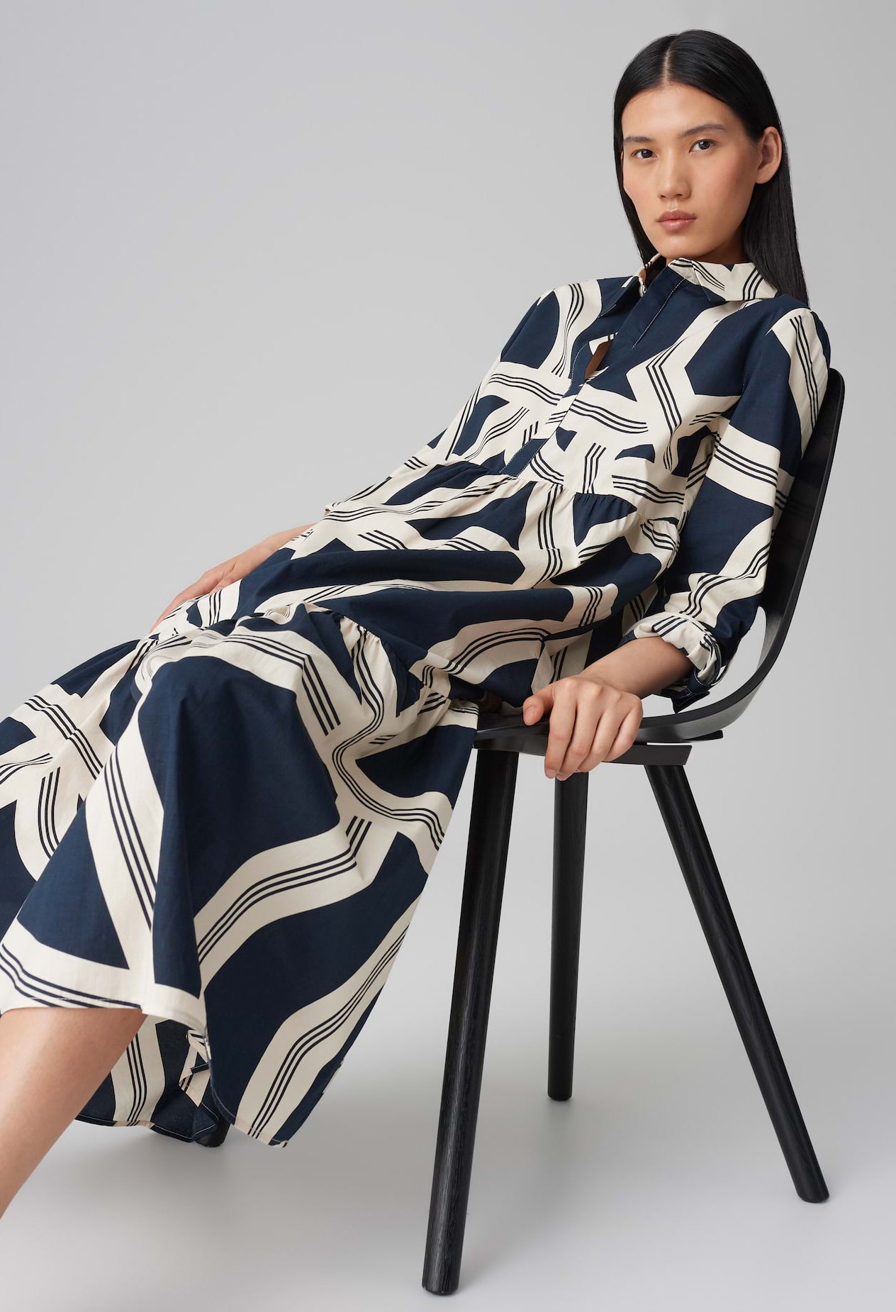 Woman wearing a navy and white patterned dress sitting on a black chair against a gray background