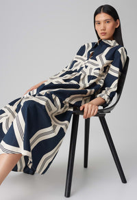 Woman wearing a navy and white patterned dress sitting on a black chair against a gray background