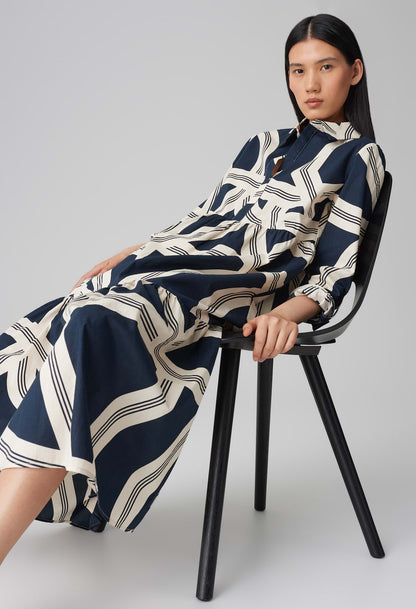 Woman wearing a navy and white patterned dress sitting on a black chair against a gray background