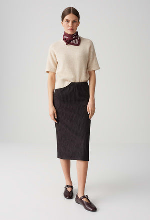 Woman wearing a beige sweater and black skirt with a red scarf on a white background