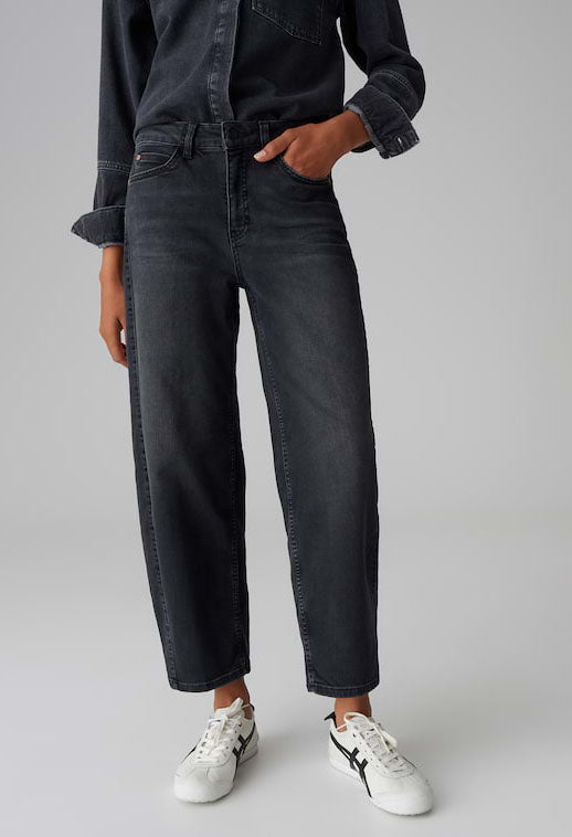 Person wearing black jeans and white sneakers on a gray background