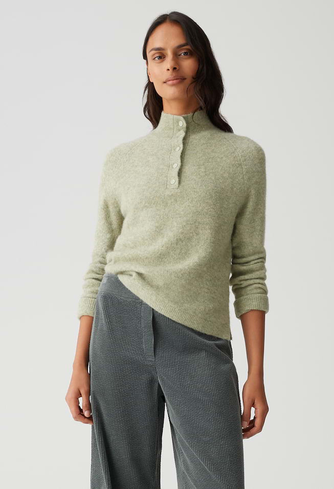 Woman wearing a light green sweater and gray pants against a white background