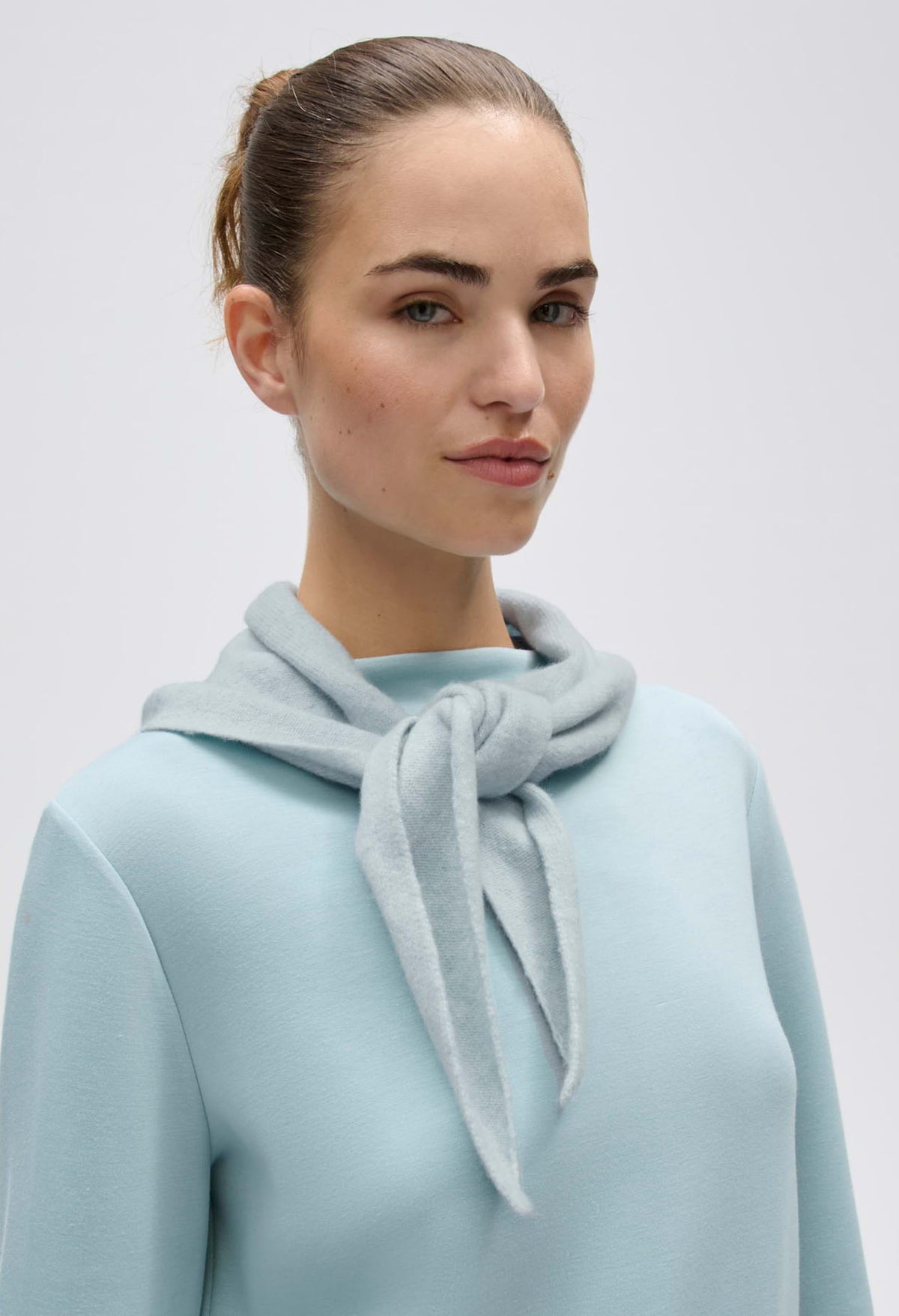 Model wearing finely knitted in a dusty aqua color as a triangular scarf. 
