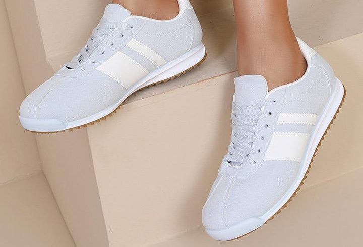 White sneakers with beige stripes worn by a person on a beige background