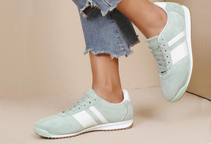 Light green sneakers with white stripes worn by a person on a beige background