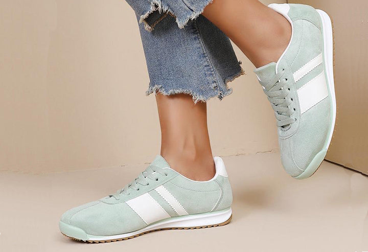 Light green sneakers with white stripes worn by a person on a beige background