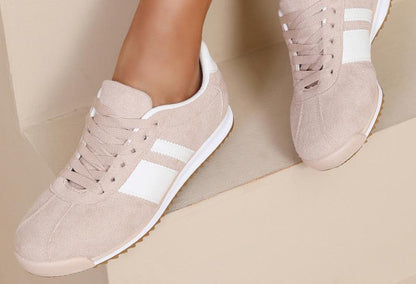 Beige sneakers with white stripes worn by a person on a beige background