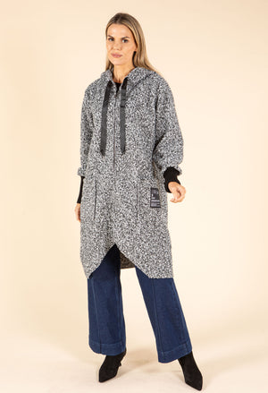 Woman wearing a long, patterned coat over a dress with blue pants on a beige background