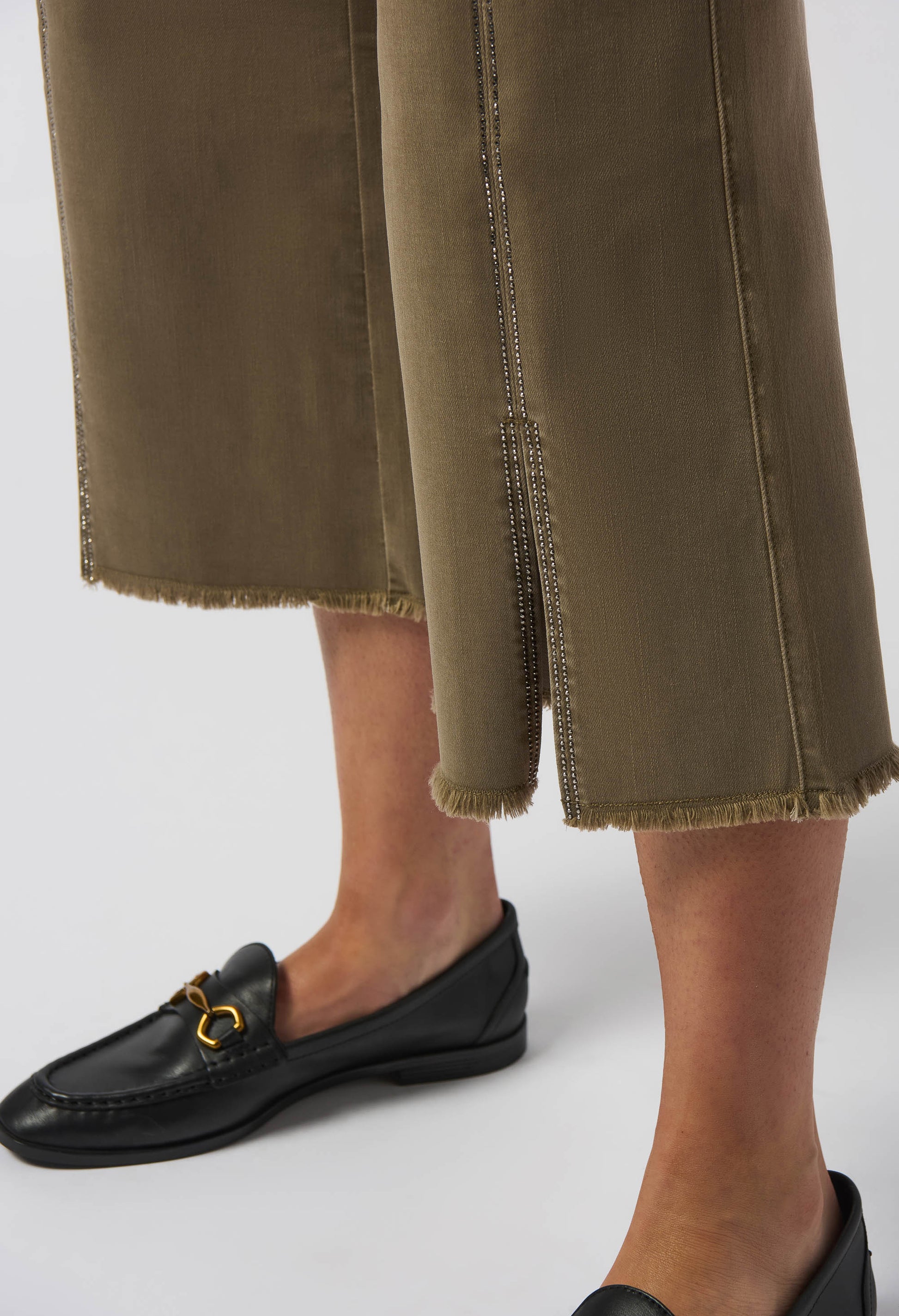 Person wearing olive green pants and black loafers on a white background