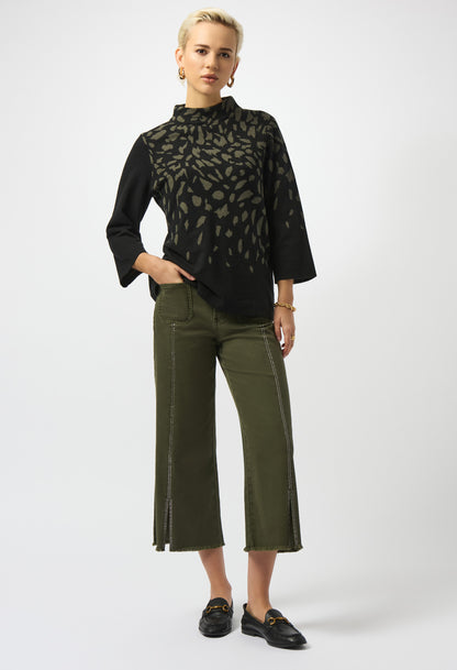 Woman wearing a black blouse with a pattern and green pants on a white background