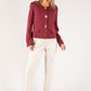 Woman wearing a burgundy jacket and white pants on a white background