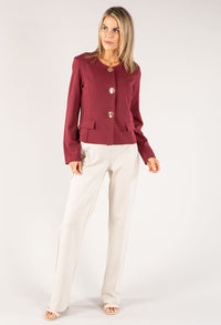 Woman wearing a burgundy jacket and white pants on a white background