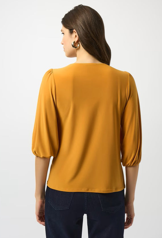 Woman wearing a mustard yellow blouse with navy pants on a white background