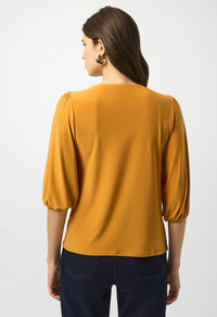 Woman wearing a mustard yellow blouse with navy pants on a white background