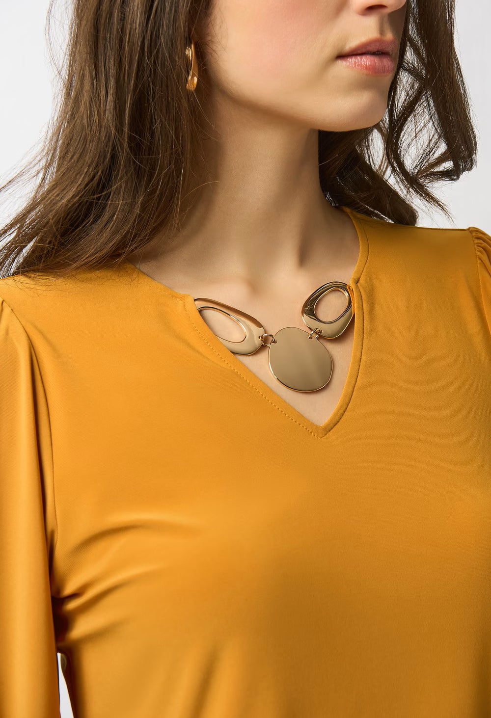 Woman wearing a mustard yellow top with a necklace on a white background