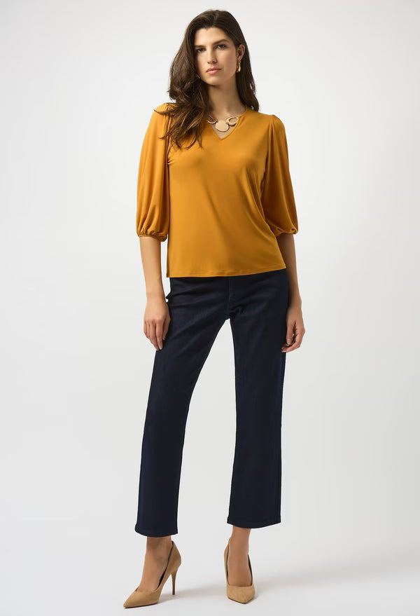 Woman wearing a mustard yellow top and navy pants on a white background