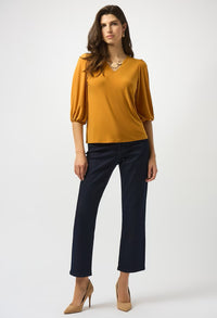 Woman wearing a mustard yellow top and navy pants on a white background