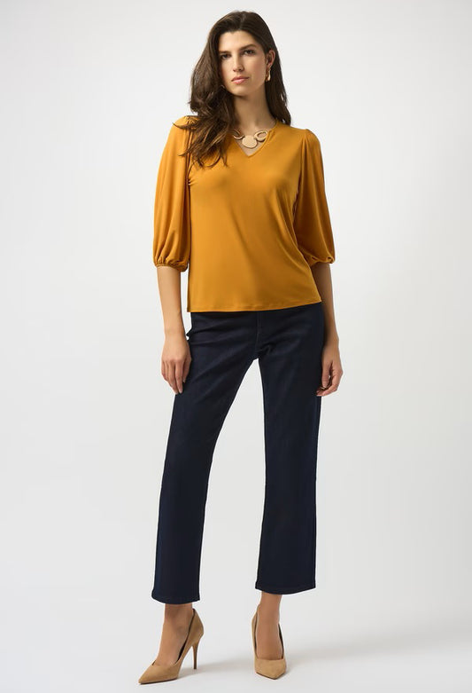 Woman wearing a mustard yellow top and navy pants on a white background