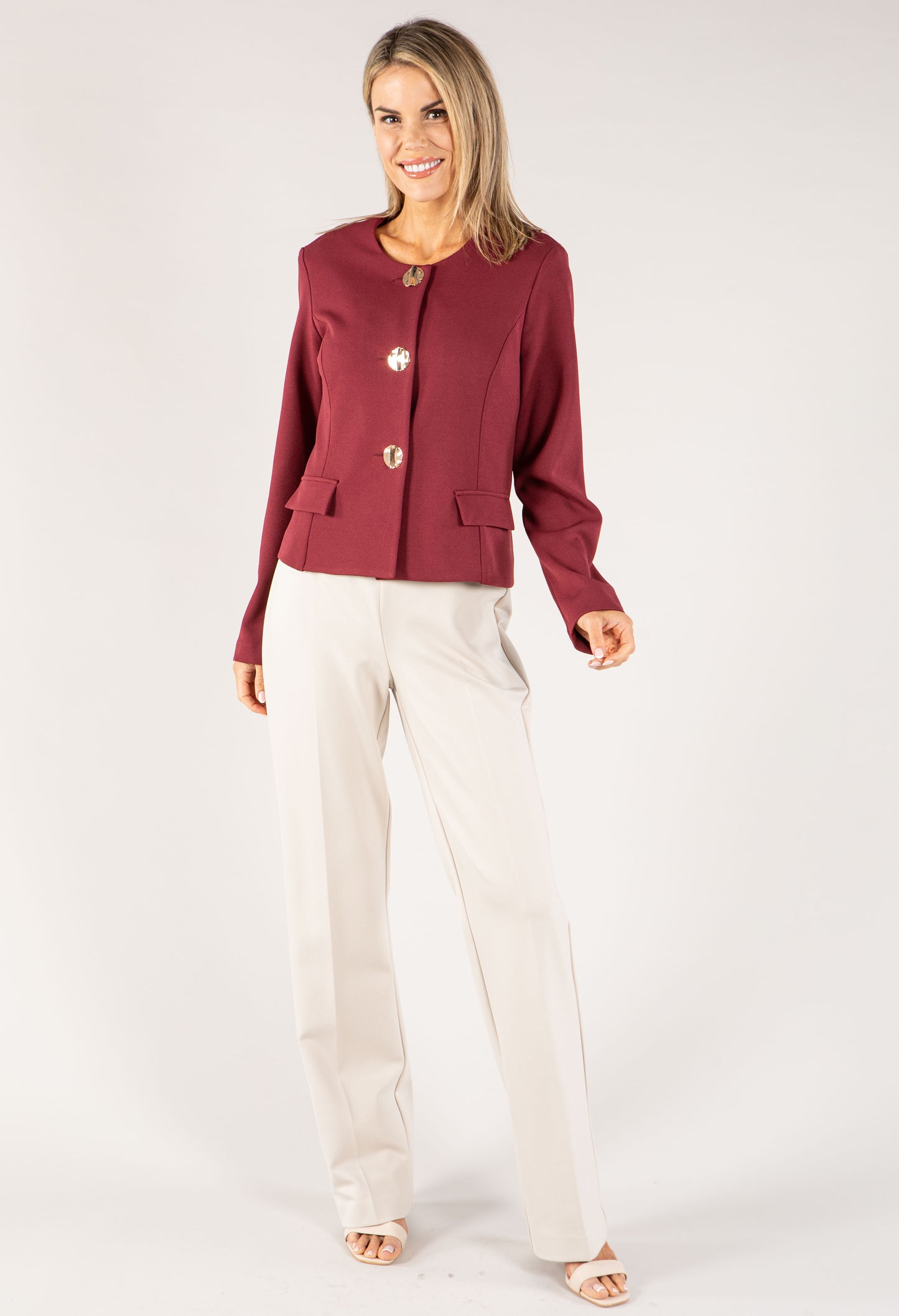 Woman wearing a burgundy blazer and white pants on a white background
