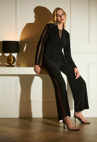 Woman in a black suit sitting on a white surface with a lamp in the background