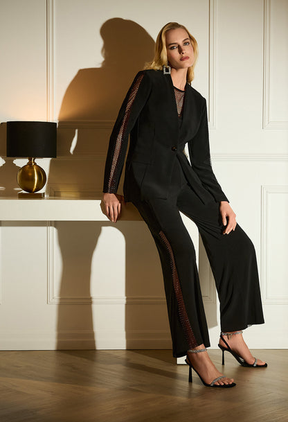 Woman in a black suit sitting on a white surface with a lamp in the background