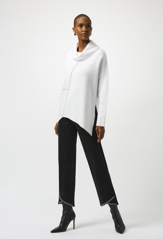 Woman wearing a white cowl-neck sweater and black pants on a white background