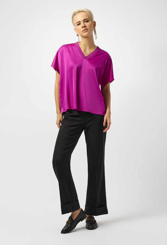Woman wearing a bright pink top and black pants on a white background