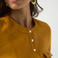 Close-up of a person wearing gold earrings and a mustard yellow top with button details.