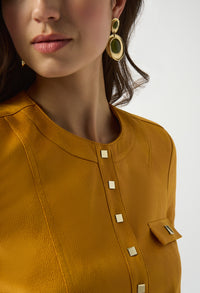 Close-up of a person wearing gold earrings and a mustard yellow top with button details.