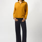 Woman wearing a mustard yellow sweater and dark blue pants on a white background