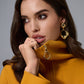 Woman wearing a mustard yellow coat with gold earrings against a gray background