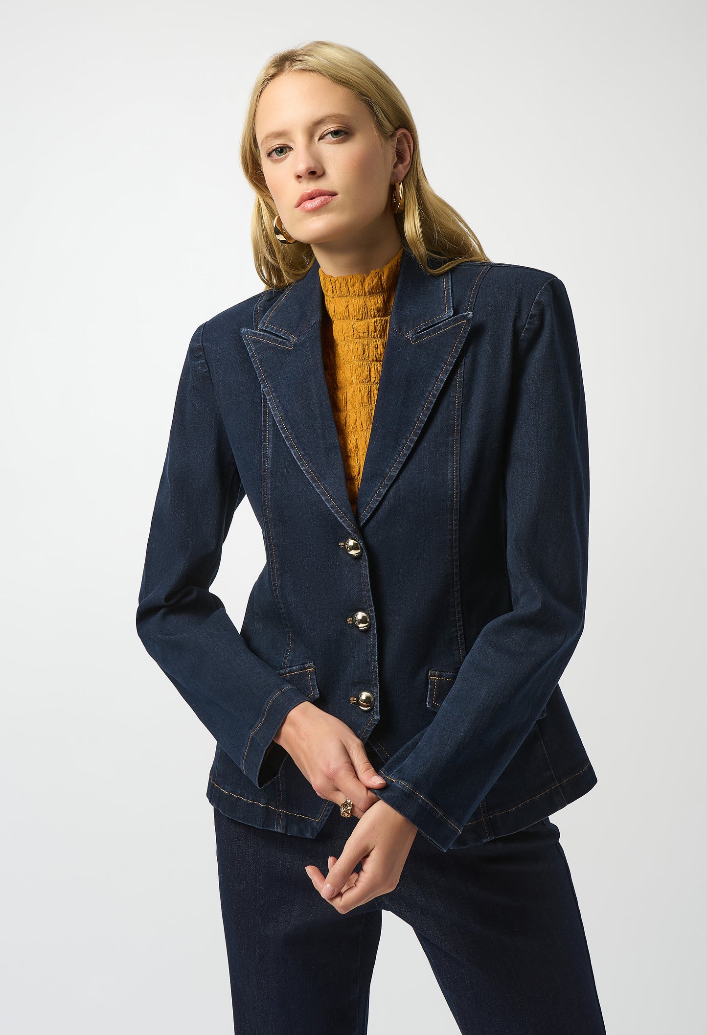 Woman wearing a navy blue blazer over a mustard yellow sweater on a white background