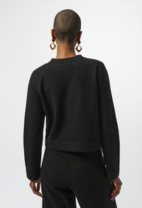 Person wearing a black sweater and pants on a white background