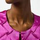 Close-up of a person wearing a bright pink satin top with a blurred background