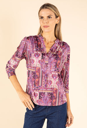 Woman wearing a purple patterned blouse against a beige background