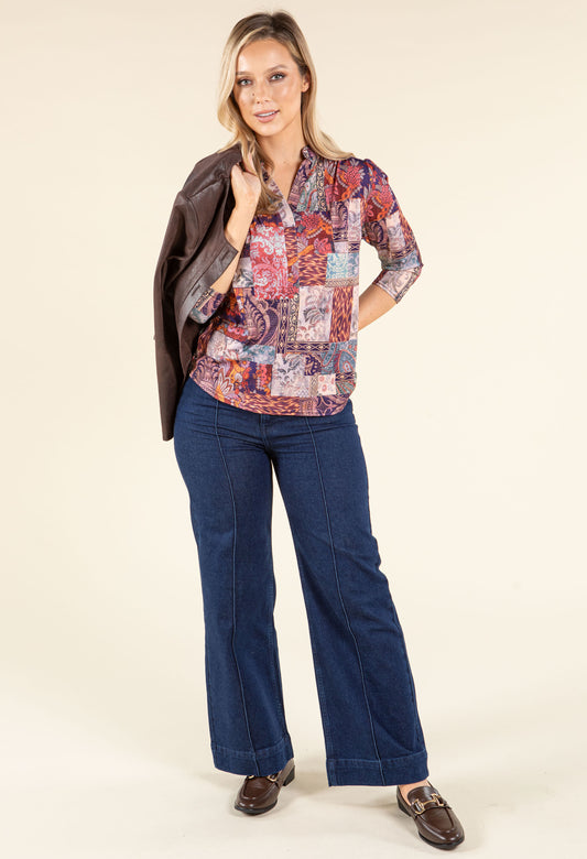 Woman in a stylish outfit with a jacket, patterned shirt, and jeans walking outdoors.