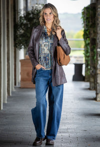 Woman in a stylish outfit with a jacket, patterned shirt, and jeans walking outdoors.