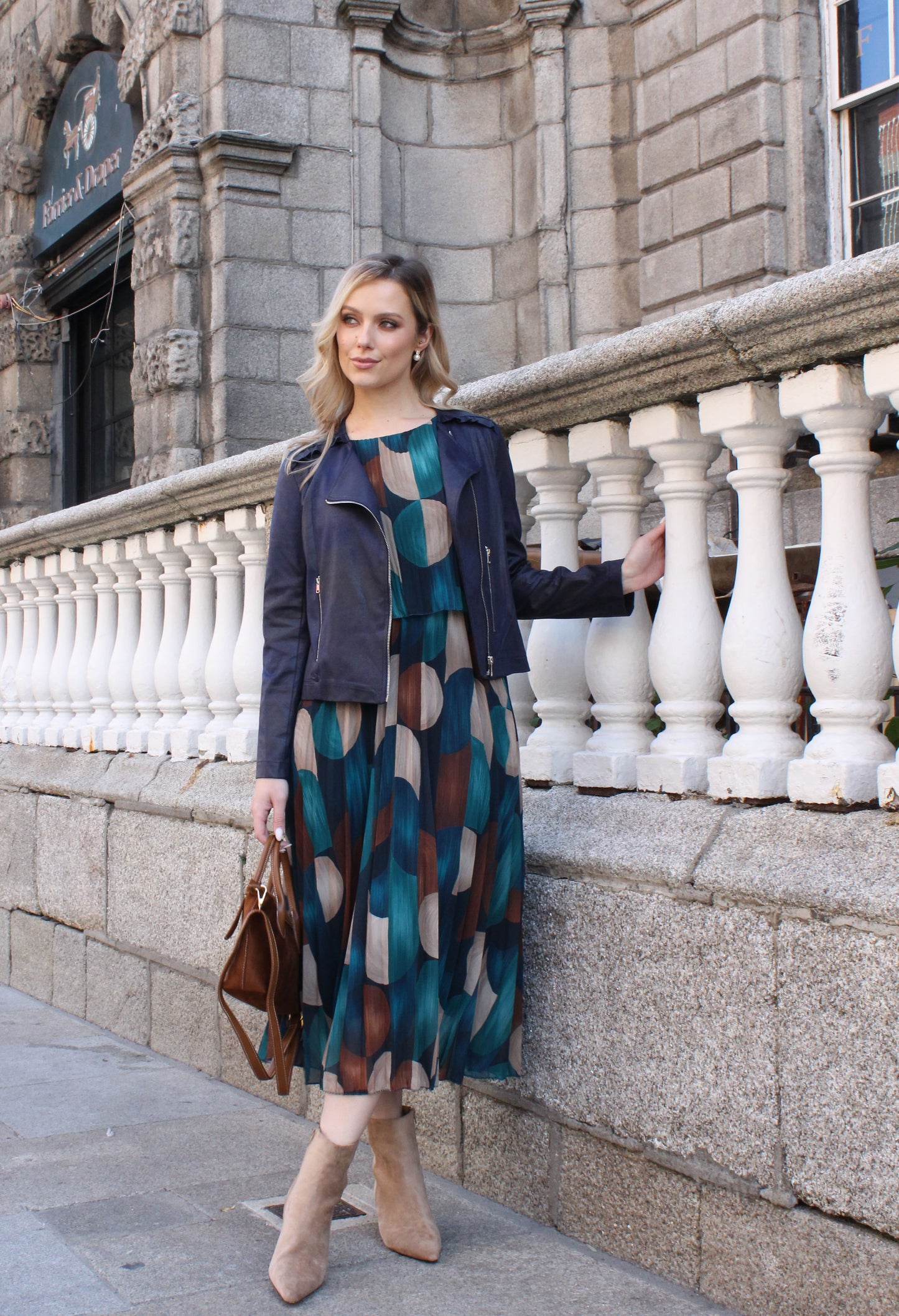 Woman in a patterned dress standing on a stone balcony with a building in the background