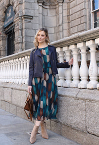 Woman in a patterned dress standing on a stone balcony with a building in the background