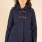 Woman wearing a navy blue coat with brown buttons on a beige background
