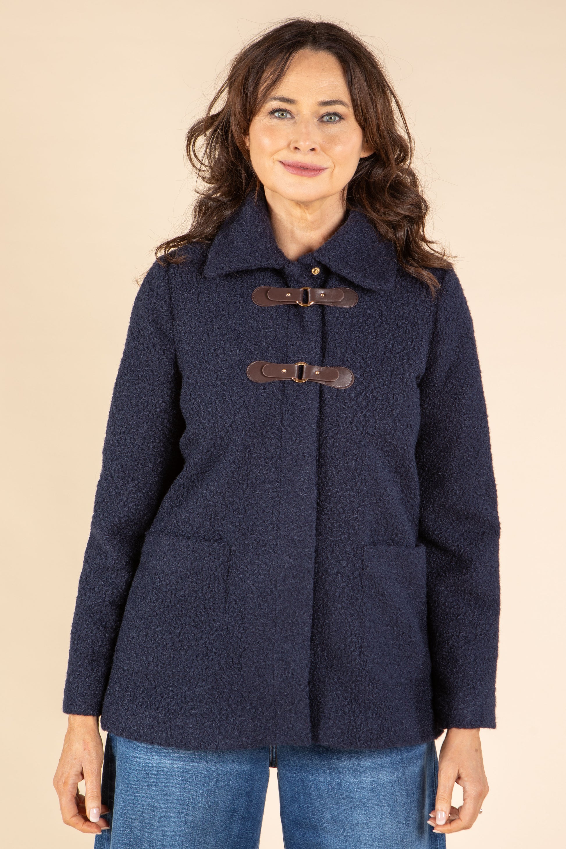Woman wearing a navy blue coat with brown buttons on a beige background