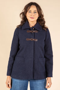 Woman wearing a navy blue coat with brown buttons on a beige background