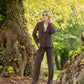 Woman in a brown suit standing in a park with trees and greenery.