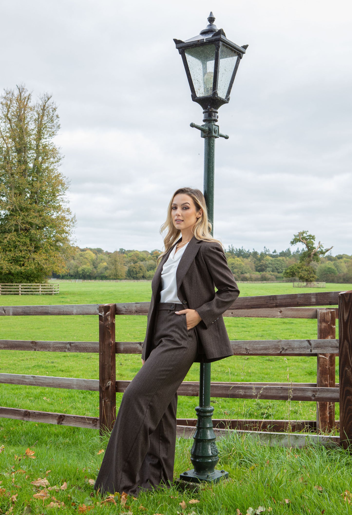 Woman in a brown suit standing next to a lamp post in a field