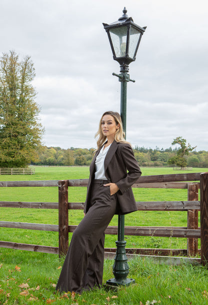 Woman in a brown suit standing next to a lamp post in a field