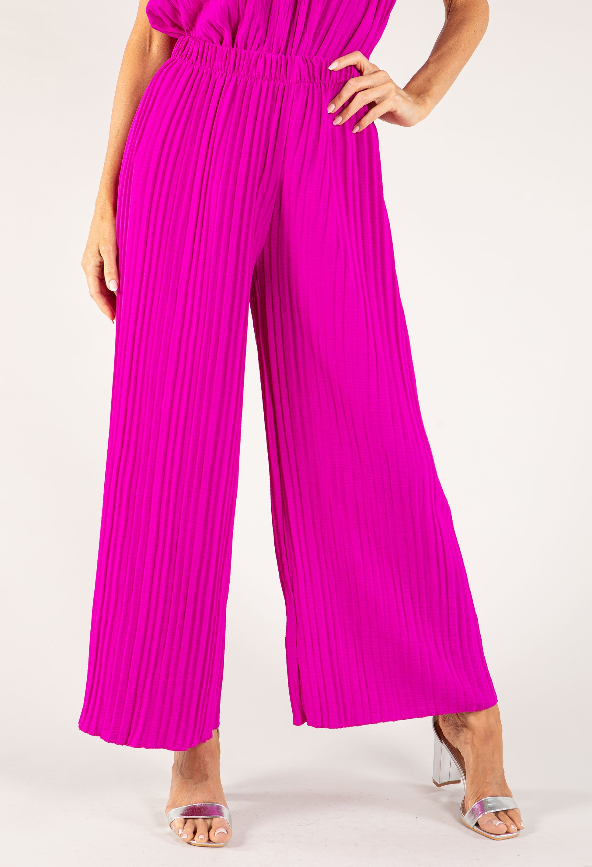 Person wearing a bright pink pleated jumpsuit on a white background