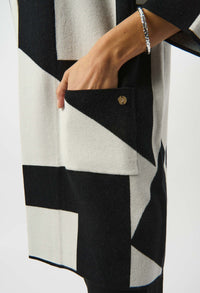 Close-up of a person wearing a black, white, and gray patterned cardigan with a button on a white background.