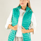 Woman wearing a teal puffer vest over a white shirt on a light gray background