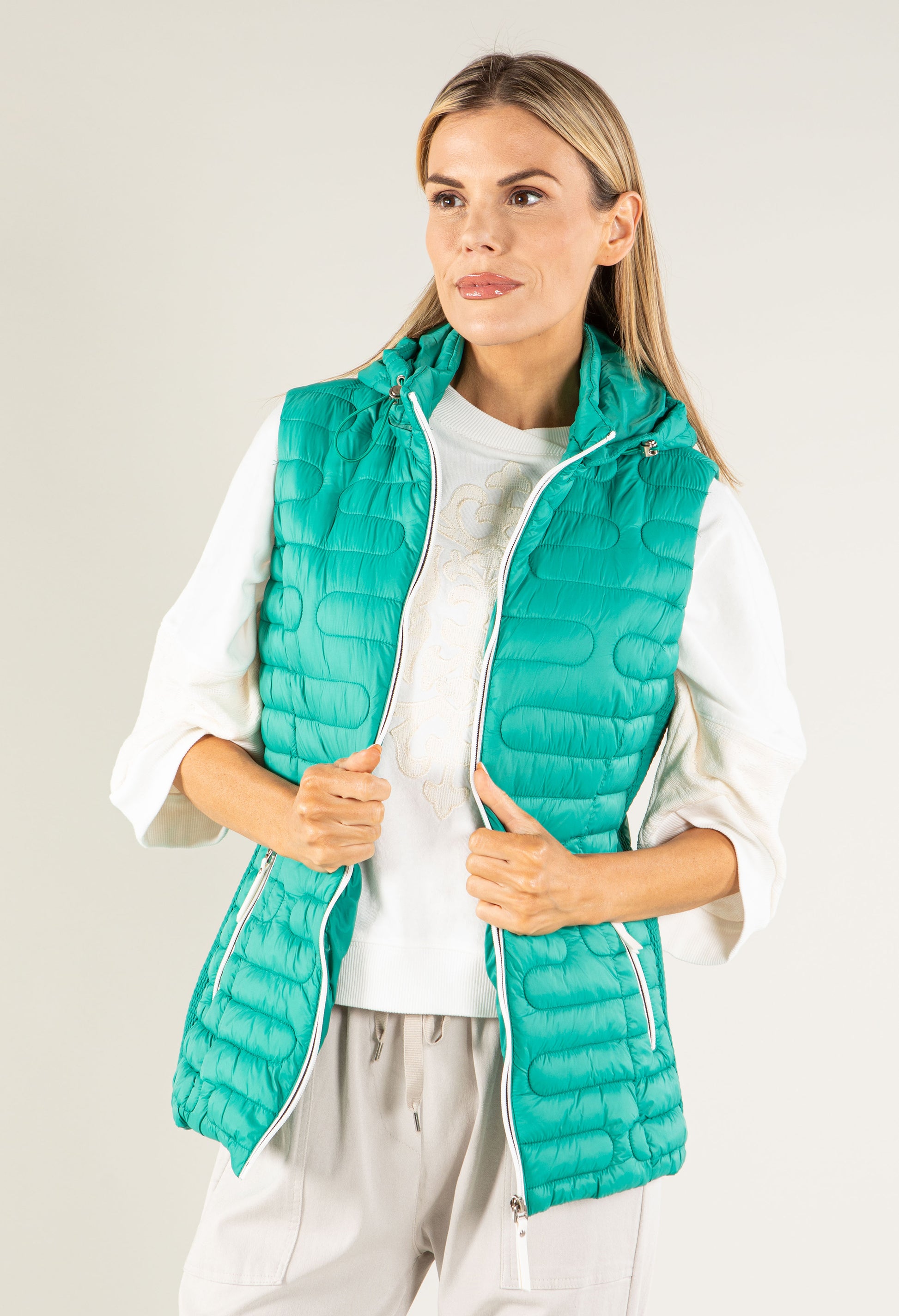 Woman wearing a teal puffer vest over a white shirt on a light gray background