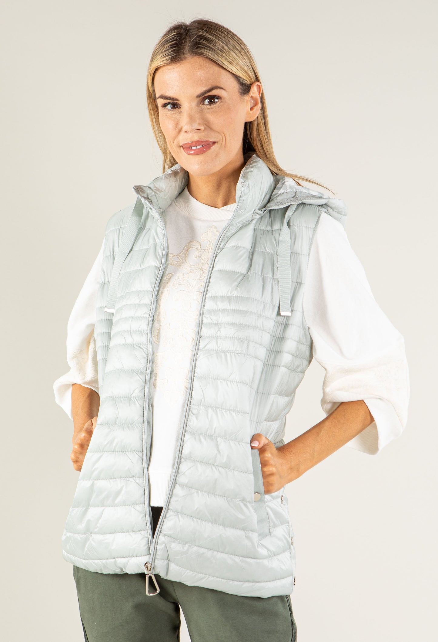 Woman wearing a light gray puffer vest over a white shirt on a plain background